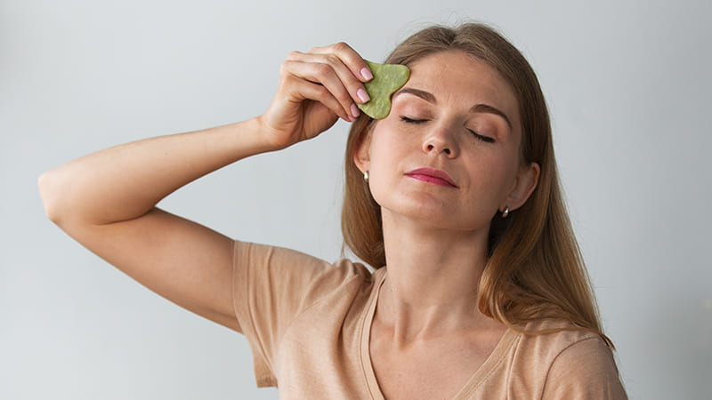 Mujer haciendo yoga facial con herramienta de jade